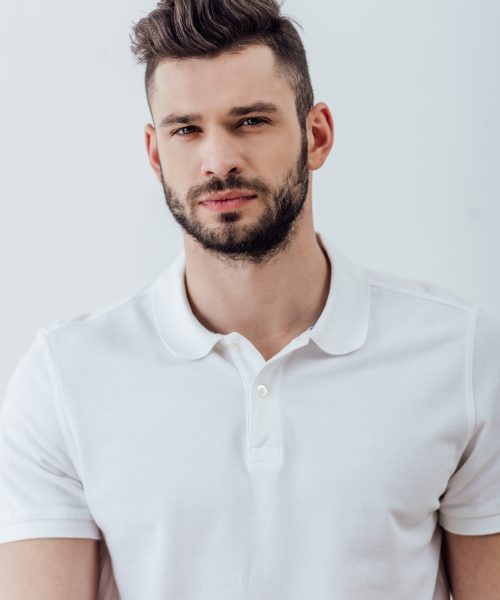 handsome bearded man in white polo shirt looking at camera isolated on grey